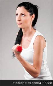 sporty woman is exercising with red barbell on grey background