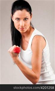 sporty woman is exercising with red barbell on grey background and looking at camera