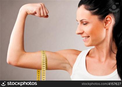 sporty woman is measuring her biceps on grey background