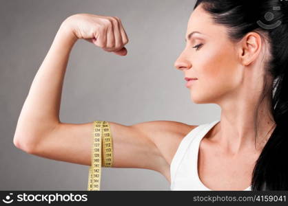 sporty woman is measuring her biceps on grey background