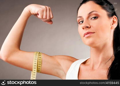 sporty woman is measuring her biceps on grey background