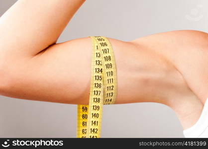 sporty woman is measuring her biceps on grey background