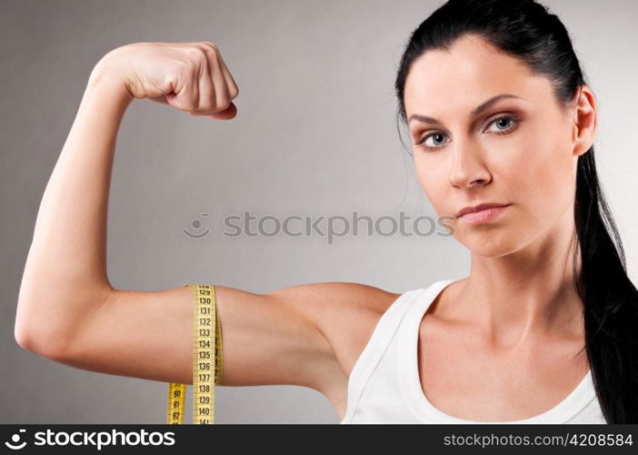 sporty woman is measuring her biceps on grey background