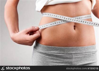sporty woman is measuring her waist on grey background