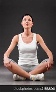 sporty woman is relaxing in lotus pose on grey background