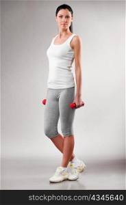 sporty woman is standing with barbells on grey background