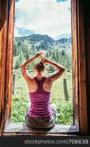 Sporty woman on hiking trip is enjoying the view, sitting on the floor of a mountain chalet