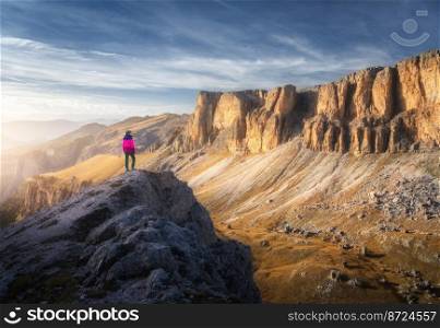 Sporty woman on the mountain peak and mountain canyon at sunset. Autumn in Dolomites, Italy. Colorful landscape with girl on the cliff, high rocks, blue sky in fall. Trekking and hiking. Top view. Sporty woman on the mountain peak and mountain canyon
