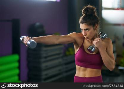 Sporty woman punching and boxing with dumbbells. Hard exercising and training at the gym. Fitness concept.. Sporty woman punching and boxing with dumbbells.