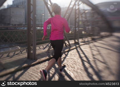 sporty woman running on sidewalk at early morning jogging with city sunrise scene in background