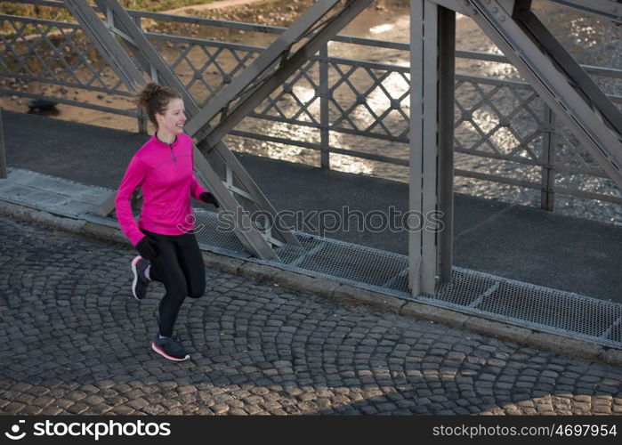 sporty woman running on sidewalk at early morning jogging with city sunrise scene in background