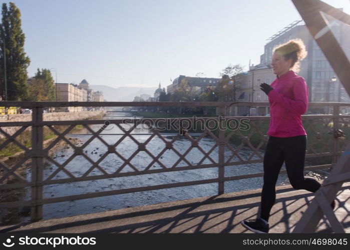 sporty woman running on sidewalk at early morning jogging with city sunrise scene in background