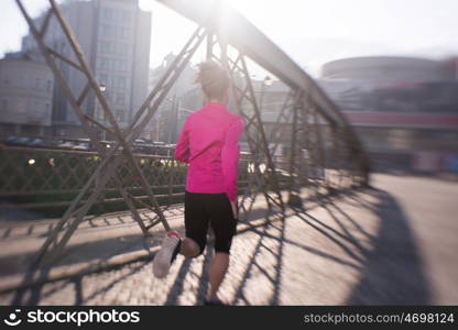 sporty woman running on sidewalk at early morning jogging with city sunrise scene in background