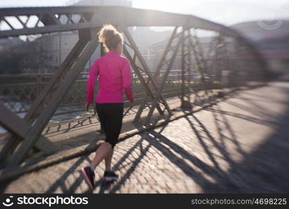 sporty woman running on sidewalk at early morning jogging with city sunrise scene in background