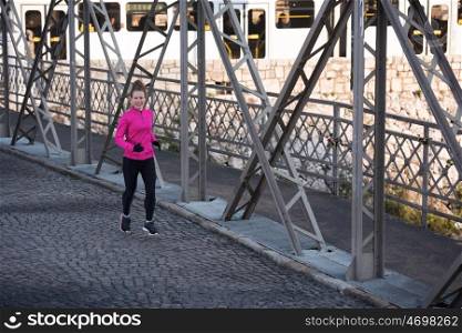 sporty woman running on sidewalk at early morning jogging with city sunrise scene in background