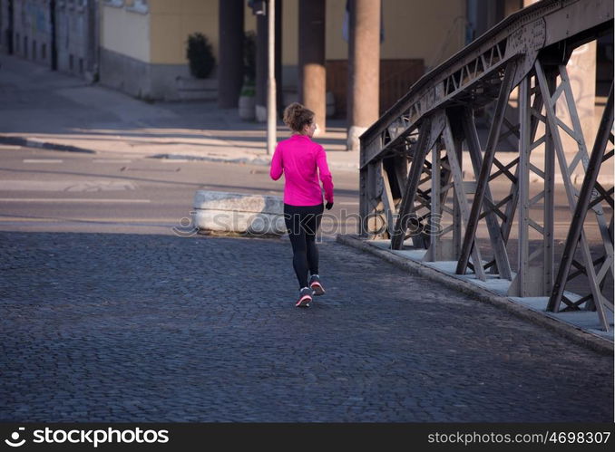 sporty woman running on sidewalk at early morning jogging with city sunrise scene in background