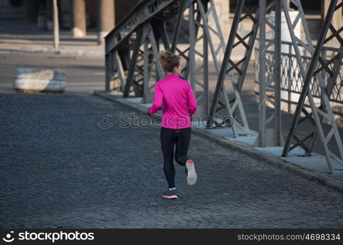 sporty woman running on sidewalk at early morning jogging with city sunrise scene in background