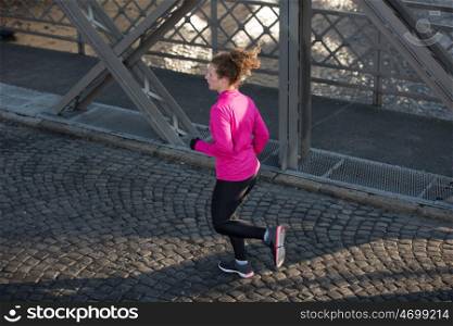 sporty woman running on sidewalk at early morning jogging with city sunrise scene in background