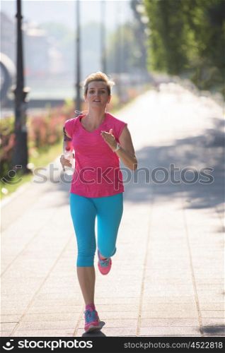 sporty woman running on sidewalk at early morning with city sunrise scene in background