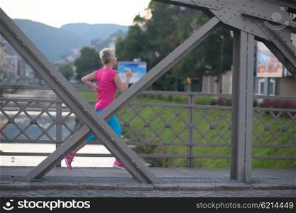 sporty woman running on sidewalk at early morning with city sunrise scene in background