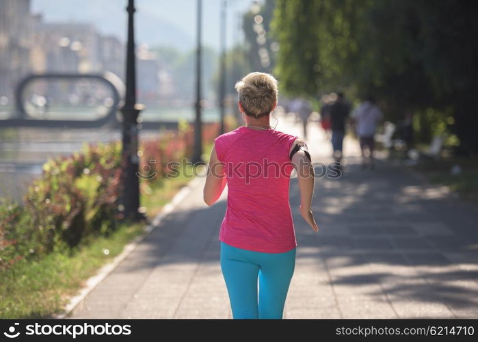 sporty woman running on sidewalk at early morning with city sunrise scene in background