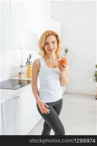 Sporty woman throws up an orange, fit breakfast on the kitchen. Female person at home in the morning, healthy nutrition and lifestyle. Woman throws up an orange, fit breakfast