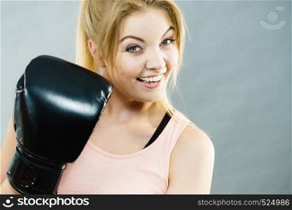 Sporty woman wearing black boxing gloves, fighting. Studio shot on grey background.. Happy smiling woman wearing boxing gloves