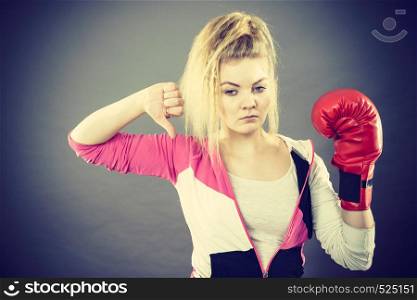 Sporty woman wearing red boxing gloves showing thumb down gesture. Studio shot on dark background.. Woman wearing boxing gloves showing thumb down
