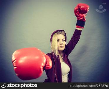 Sporty woman wearing red boxing gloves, winning fight, being motivated feeling relief and happiness. Studio shot on dark background.. Woman winner wearing boxing gloves