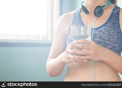 Sporty woman with headphones on her neck drinking water, Healthy diet concept