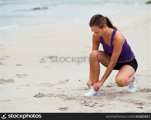 Sporty young woman doing her laces on the sea coast