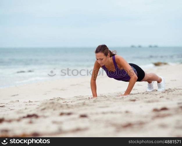 Sporty young woman doing push ups on the sea coast