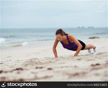 Sporty young woman doing push ups on the sea coast