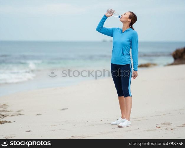 Sporty young woman drinking water on the sea coast