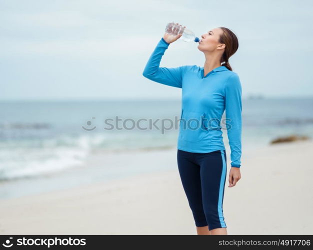 Sporty young woman drinking water on the sea coast