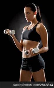 Sporty young woman holding dumbbells on black background