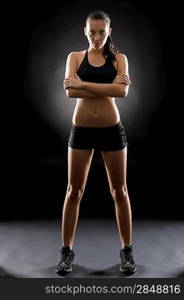 Sporty young woman standing with arms crossed on black background
