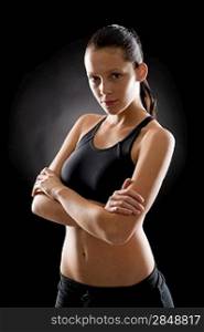 Sporty young woman standing with arms crossed on black background