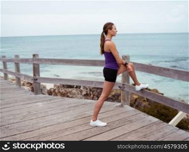 Sporty young woman stretching on the sea coast