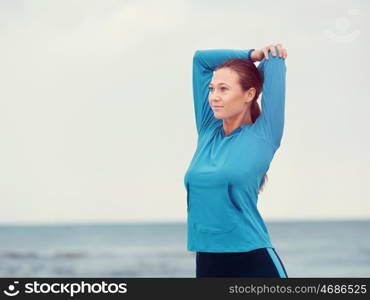 Sporty young woman stretching on the sea coast