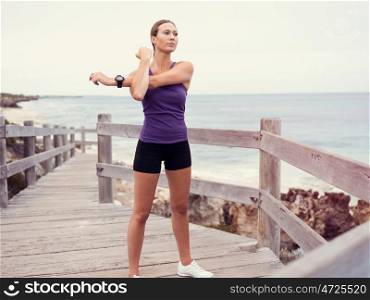 Sporty young woman stretching on the sea coast