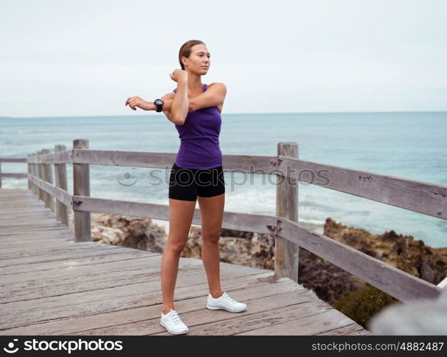 Sporty young woman stretching on the sea coast