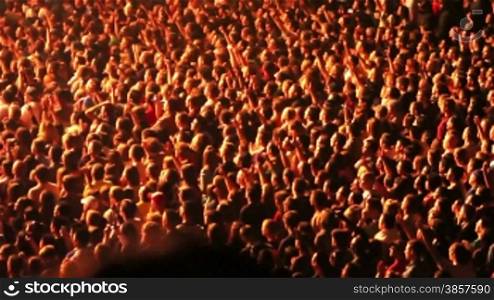 Spotlights illuminate sections of a crowd of cheering fans at a rock concert. Lights get bright at the end.