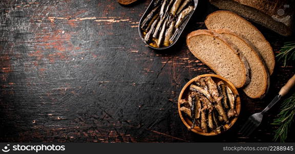 Sprats with slices of fresh bread. Against a dark background. High quality photo. Sprats with slices of fresh bread.