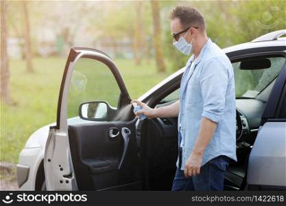 Spraying antibacterial sanitizer spray on car, infection control concept. Prevent Coronavirus, COVID-19, flu. Man wearing in medical protective mask driving a car. Disinfecting wipes. Spraying antibacterial sanitizer spray on car, infection control concept. Prevent Coronavirus, COVID-19, flu. Man wearing in medical protective mask driving a car. Disinfecting wipes.