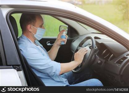 Spraying antibacterial sanitizer spray on steering wheel car, infection control concept. Prevent Coronavirus, COVID-19, flu. Disinfecting wipes. Man wearing in medical protective mask driving a car.. Spraying antibacterial sanitizer spray on steering wheel car, infection control concept. Prevent Coronavirus, COVID-19, flu. Man wearing in medical protective mask driving a car. Disinfecting wipes.