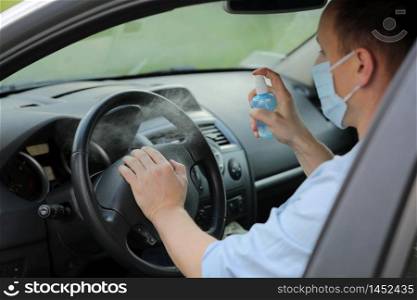 Spraying antibacterial sanitizer spray on steering wheel car, infection control concept. Prevent Coronavirus, COVID-19, flu. Man wearing in medical protective mask driving a car. Spraying antibacterial sanitizer spray on steering wheel car, infection control concept. Prevent Coronavirus, COVID-19, flu. Man wearing in medical protective mask driving a car. Disinfecting wipes.