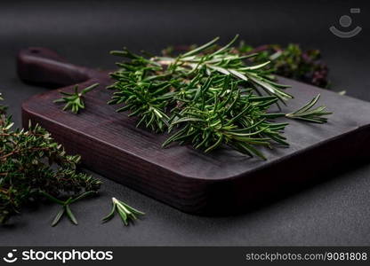 Sprigs of fresh green rosemary on a wooden cutting board on a dark concrete background