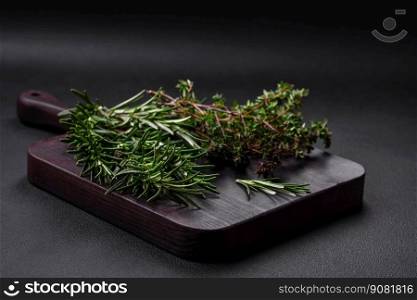 Sprigs of fresh green rosemary on a wooden cutting board on a dark concrete background