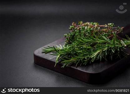 Sprigs of fresh green rosemary on a wooden cutting board on a dark concrete background